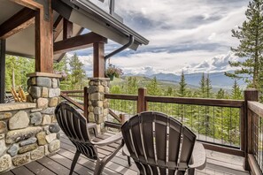 A wooden deck with stone pillars, two Adirondack chairs, and a view of mountains.