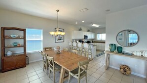 A dining area with a wooden table and chairs, a chandelier, and a kitchen in the background.