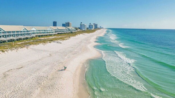A beach with a row of beach houses and a pier extending into the ocean.