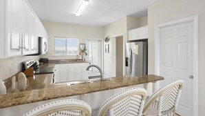 A kitchen with white cabinets, a granite countertop, a stainless steel refrigerator, and wicker chairs.