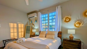 A well-lit bedroom with a large bed, a ceiling fan, a window with curtains, and a nightstand with a lamp. - 2 units | Sleeps 12 | Beach | Pool | Sunsets | Fun (Aguada)
