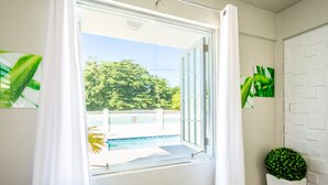 A room with a large window, a potted plant, and a white door with a geometric pattern. - 2 units | Sleeps 12 | Beach | Pool | Sunsets | Fun (Aguada)