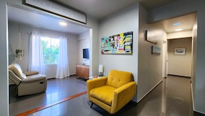 A hotel lobby with a yellow armchair, a white sofa, a wooden cabinet, and a wall with a colorful poster. - 2 units | Sleeps 12 | Beach | Pool | Sunsets | Fun (Aguada)