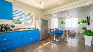 A modern kitchen with blue cabinets, a stainless steel refrigerator, and a dining area with blue chairs.