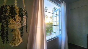 Et værelse med et vindue, en hageplante og et gardin.