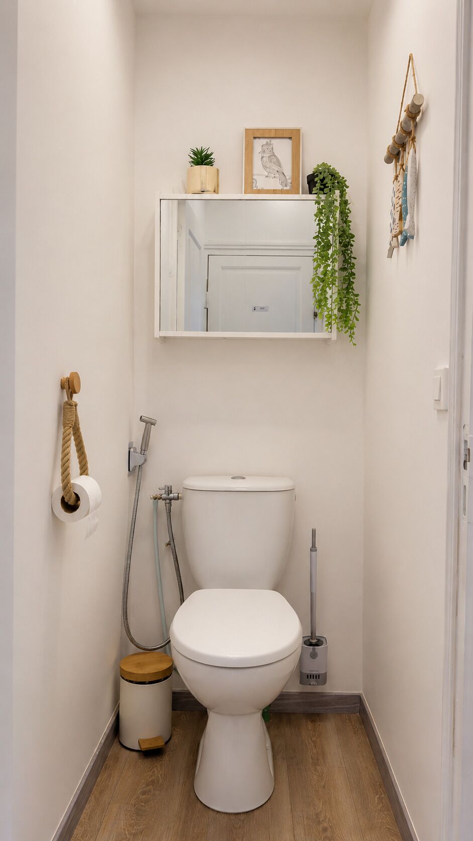 A compact bathroom with a toilet, a small trash bin, a shower, and a mirror above the toilet.