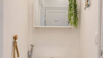 A compact bathroom with a toilet, a small trash bin, a shower, and a mirror above the toilet.