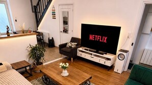 A modern living room with a sofa, a green couch, a coffee table, a TV displaying 'NETFLIX,' and a staircase. - Luxury, peaceful, 3 bedroom family home (Saint-Quentin)