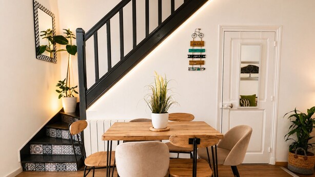 A dining area with a wooden table, four chairs, a potted plant, and a staircase with black railings. - Luxury, peaceful, 3 bedroom family home (Saint-Quentin)