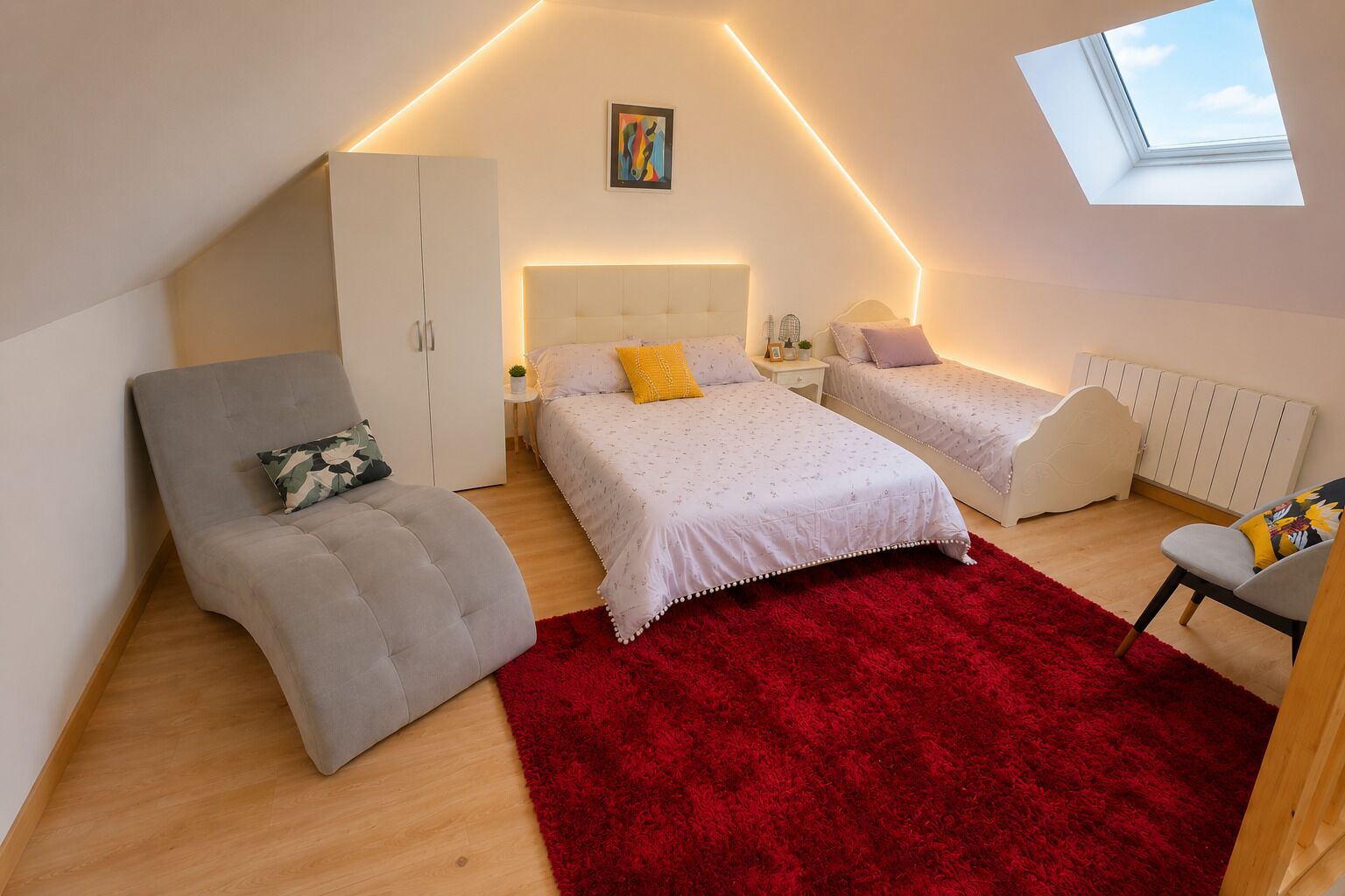 Un dormitorio con techo inclinado, un tragaluz, una cama con ropa de cama blanca, un sofá gris, un tapete rojo y una pequeña mesa con una planta.