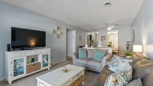 Una sala de estar moderna con un televisor de pantalla plana, una mesa de centro blanca, un sofá gris y un mueble blanco con paneles decorativos.