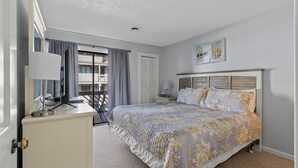 Un dormitorio con cama, escritorio, lámpara y ventana con cortinas.