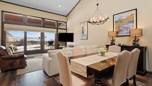 A spacious living room with a large window, a dining area with a wooden table, and a chandelier. - Mountain & Golf Course Views, & Minutes to Ski Lifts! PET FRIENDLY! (Keystone)