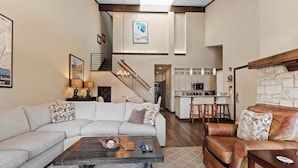 A modern living room with a sectional sofa, a leather armchair, and a coffee table. A staircase leads to a kitchen area with bar stools. - Mountain & Golf Course Views, & Minutes to Ski Lifts! PET FRIENDLY! (Keystone)