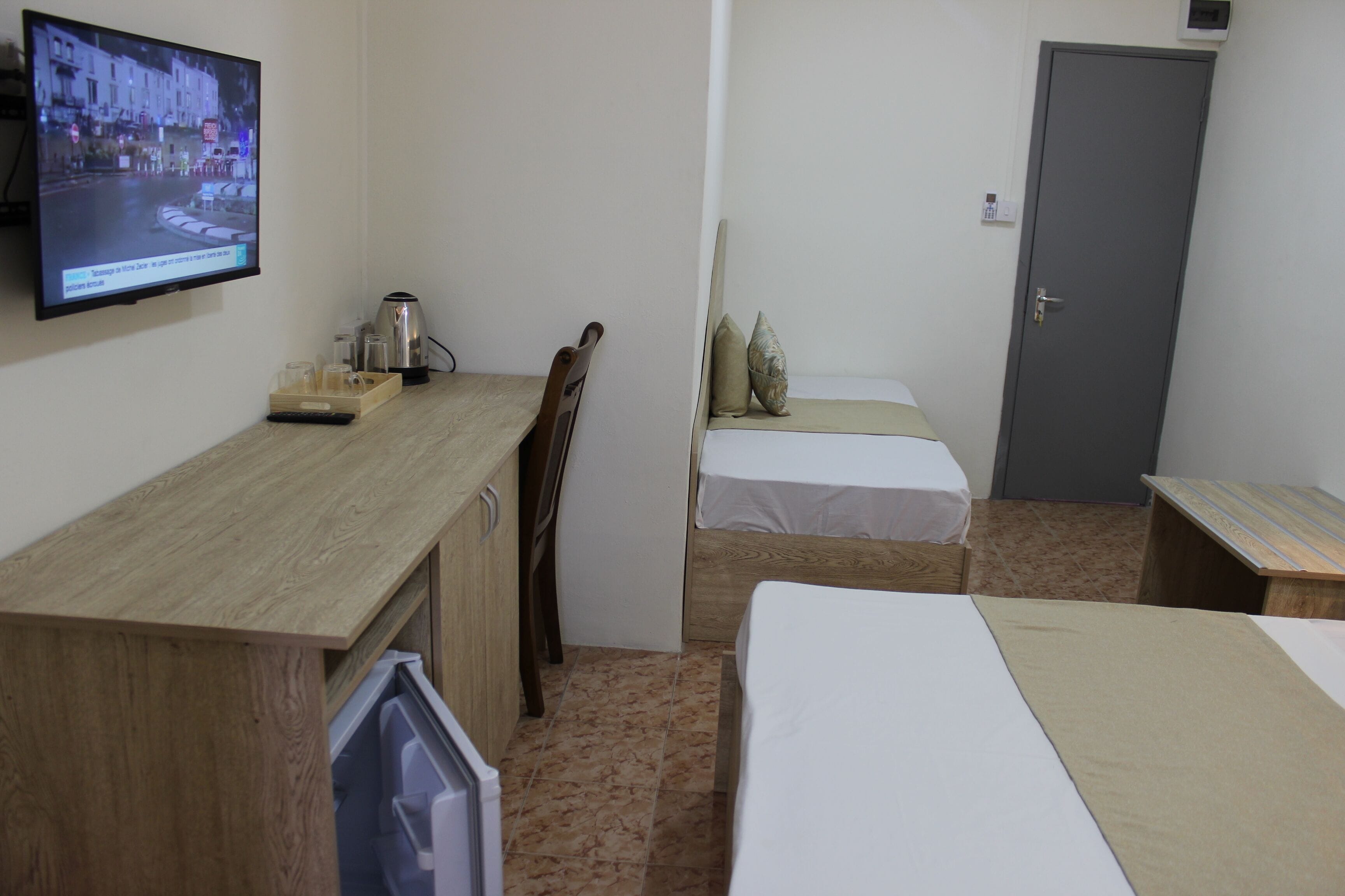 Una habitación pequeña y funcional con un escritorio de madera, una cama, una silla y un televisor montado en la pared.