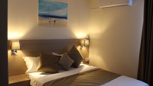 A hotel room with a neatly made bed, two bedside lamps, a painting on the wall, and an air conditioning unit. - Sikamifer Tourist Resort (Quatre Bornes)