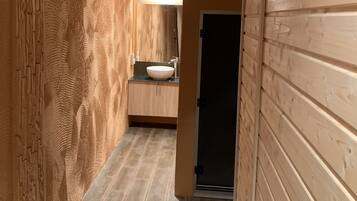 A narrow hallway with wooden paneling on both sides, a tiled floor, and a bathroom with a sink and mirror in the distance.