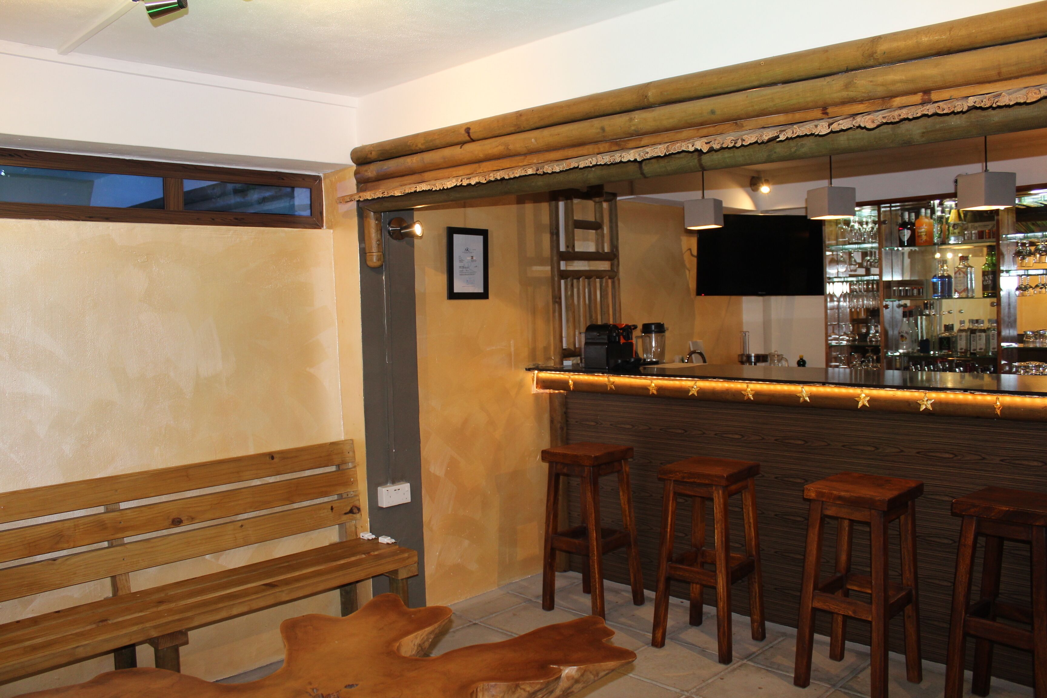 Uma área de bar com banquetas de madeira, um banco e um balcão com uma televisão acima.