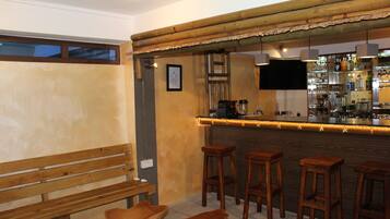 Uma área de bar com banquetas de madeira, um banco e um balcão com uma televisão acima.