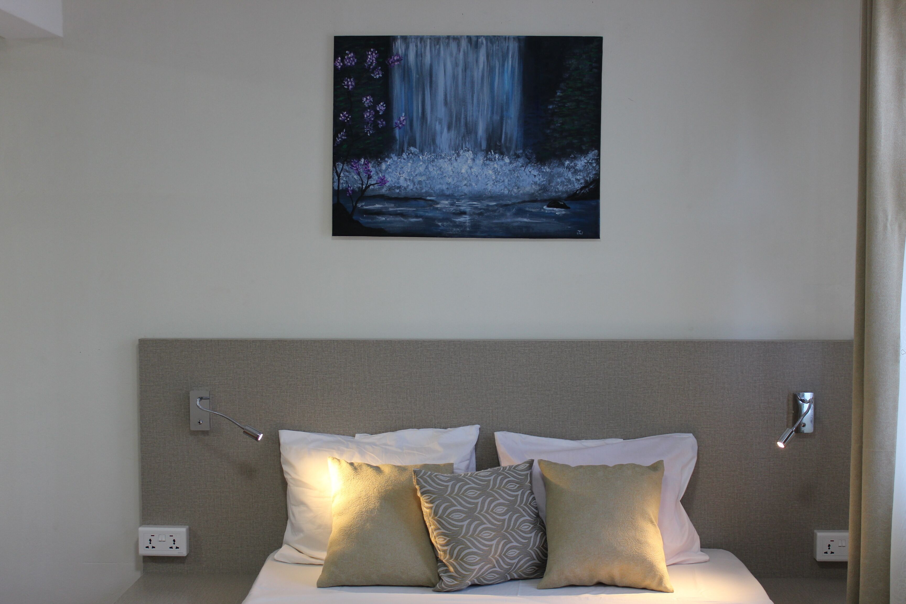 A hotel room with a bed, pillows, a wall-mounted painting of a waterfall, and a nightlight.