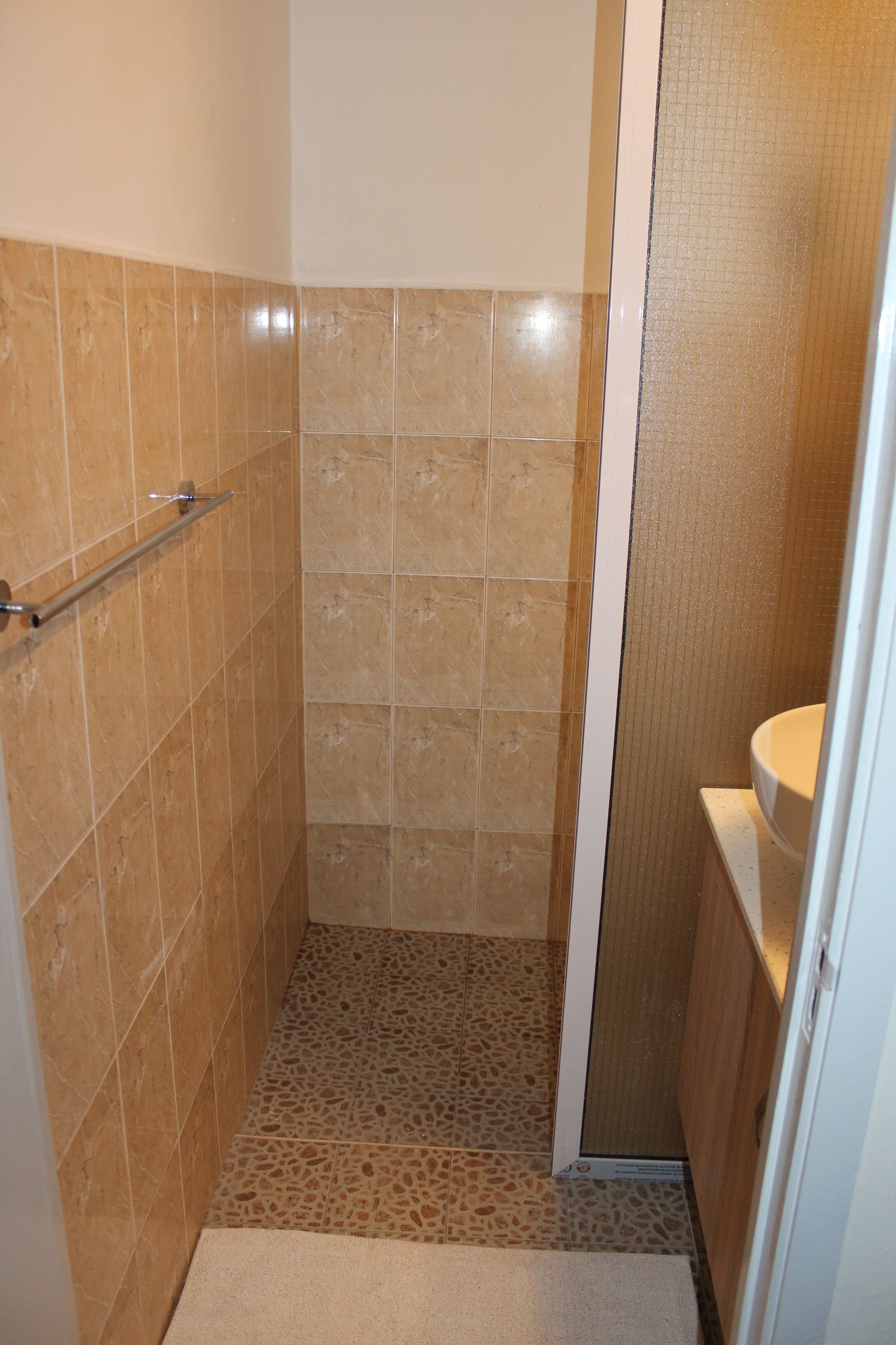 Un baño pequeño con azulejos color beige, cabina de ducha y un inodoro.