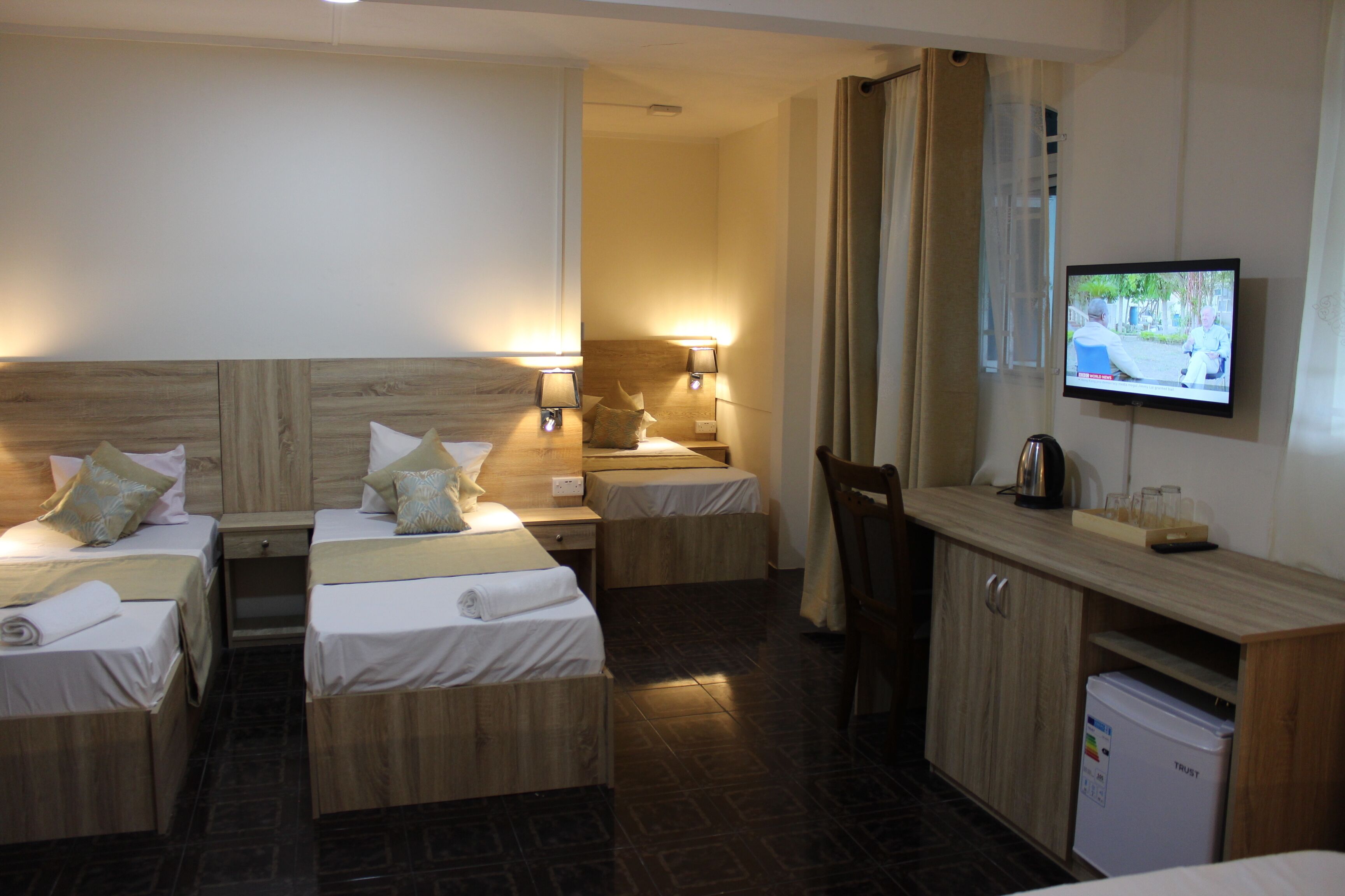 Habitación de hotel con dos camas individuales, un escritorio pequeño con televisor y un refrigerador.