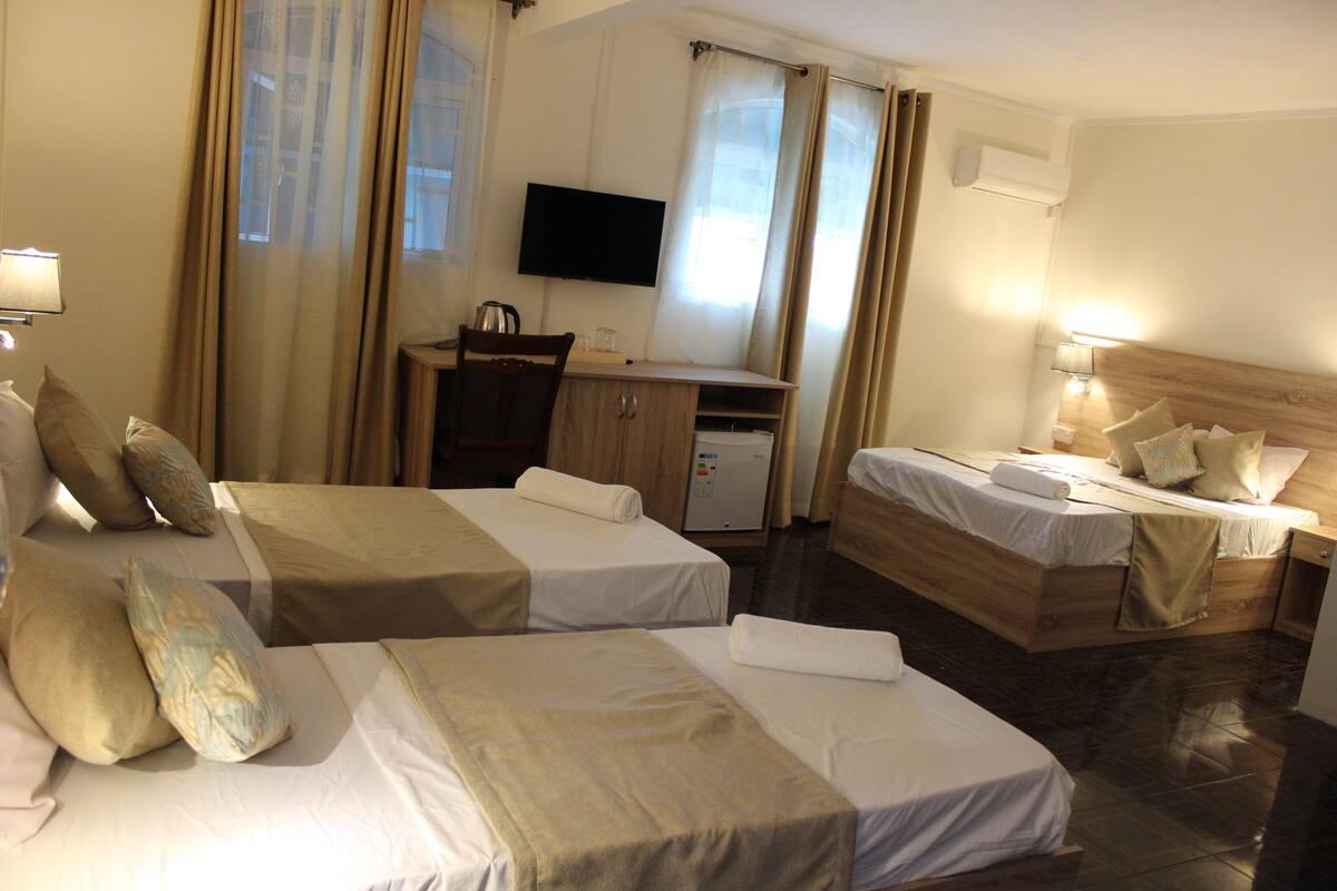 A hotel room with two beds, a desk, a TV, and a window with curtains.