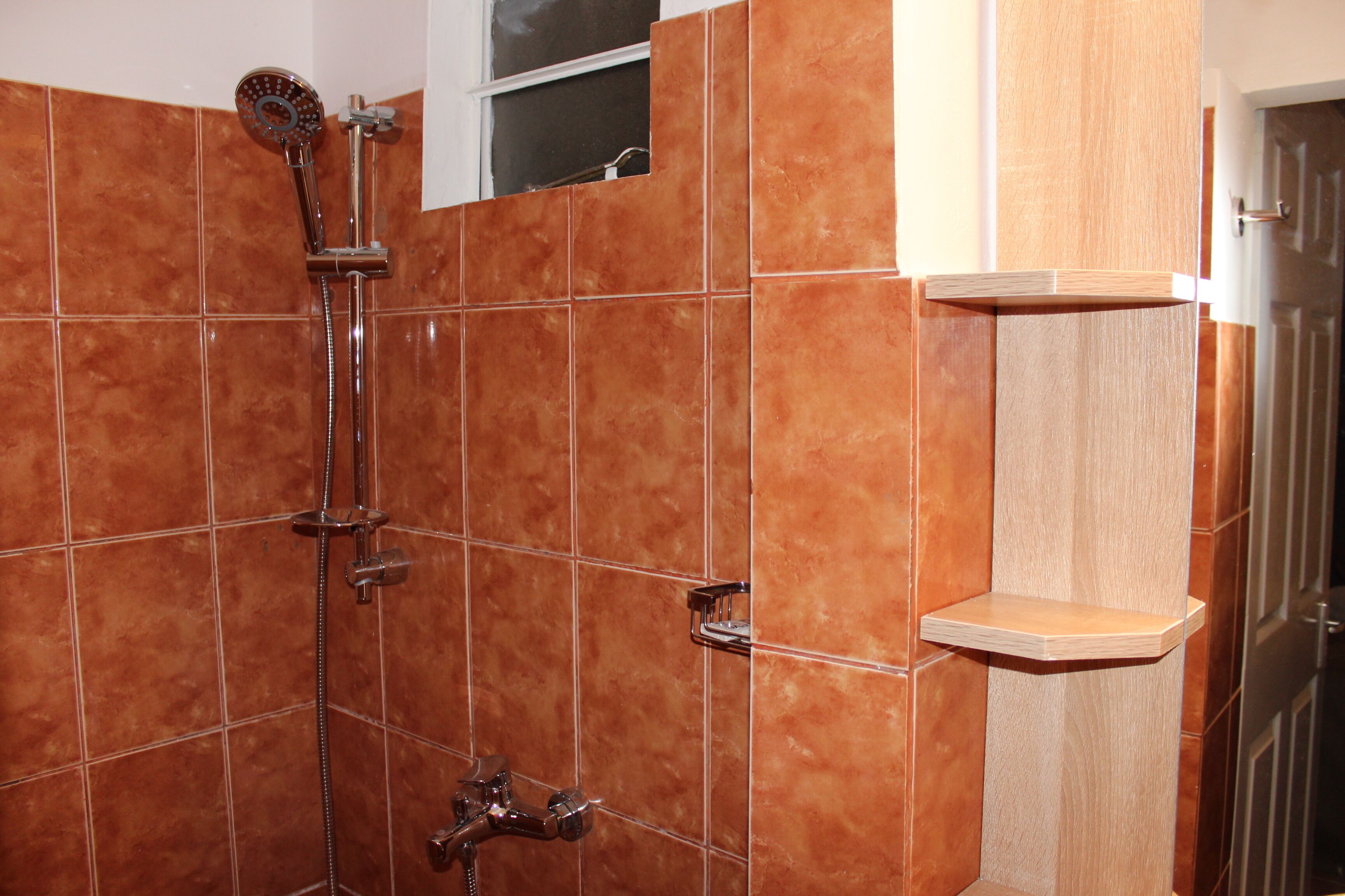 A bathroom with a shower, tiled walls, and a wooden shelf.