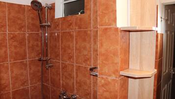 A bathroom with a shower, tiled walls, and a wooden shelf.