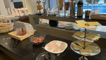A buffet setup with various food items, including a bowl of sausages, a plate of sliced meat, and several containers of coffee and condiments.