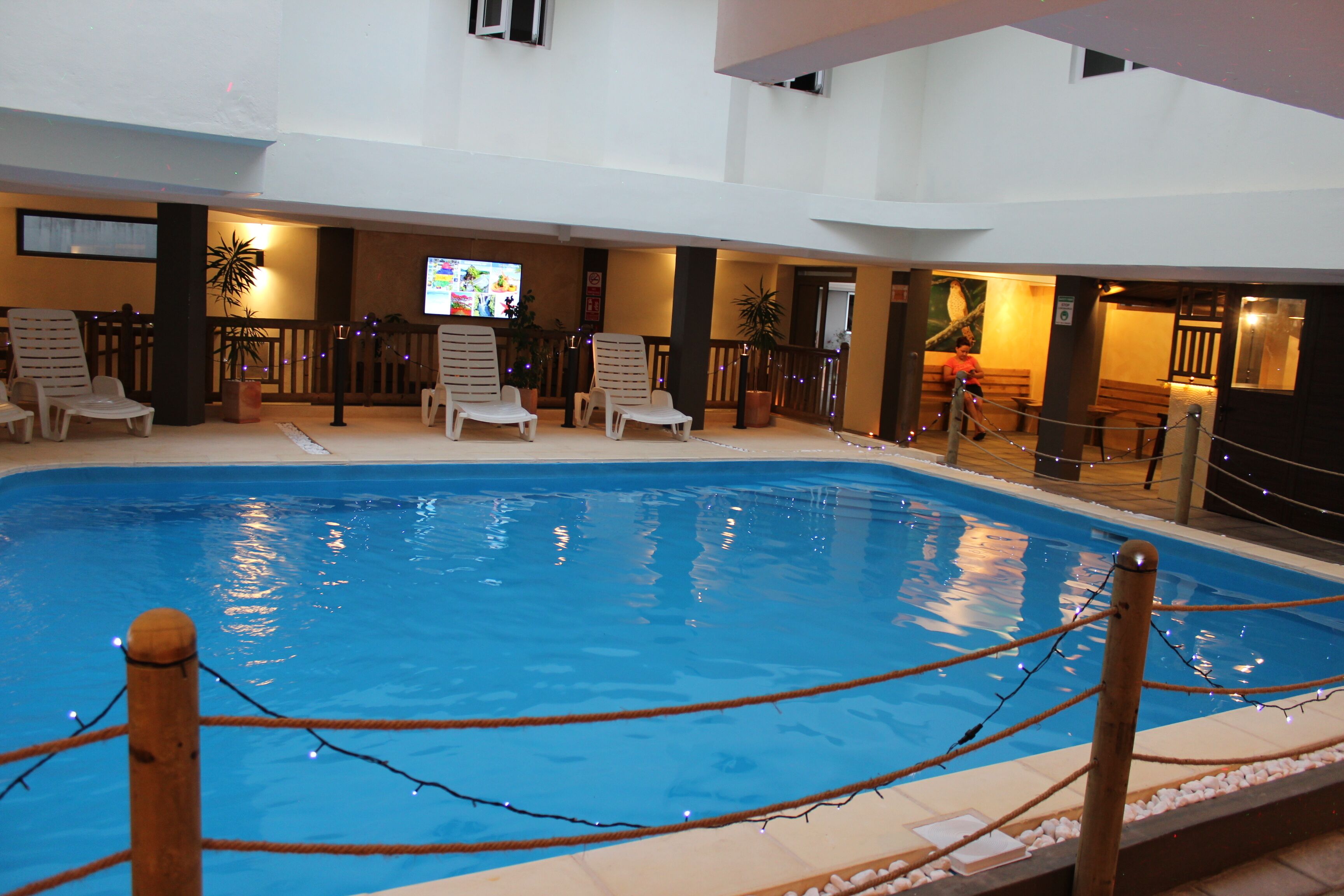 Piscina interior con sillas de descanso y una pantalla de televisión.