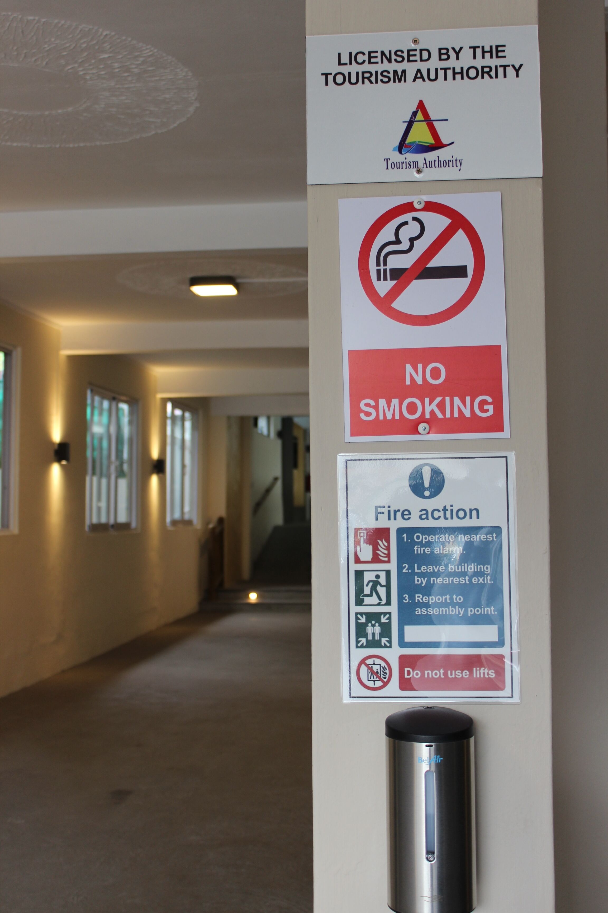 A hallway with signs indicating no smoking, fire action procedures, and a fire alarm.