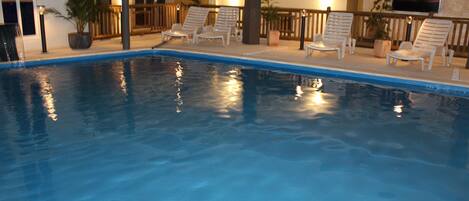 An indoor swimming pool with clear water, surrounded by lounge chairs and potted plants.