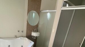 Et moderne badeværelse med et stort badekar, en bruseniche og et spejl ved håndvasken.