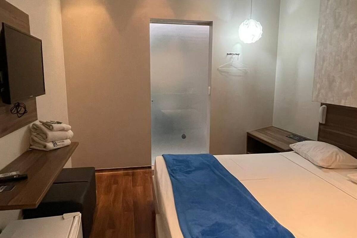 A modern hotel room with a bed, bedside table, and a small desk with a chair.