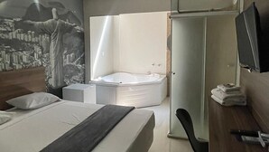 Et moderne hotelværelse med en stor seng, et skrivebord, en stol, et sminkebord med spejl og et lille opholdsområde med et bord og stole.
