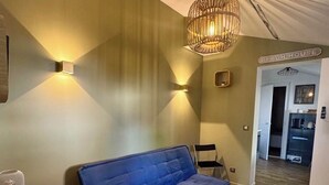 Una stanza con un divano blu, un piccolo tavolo di legno, una lampada a sospensione in vimini e un cartello che riporta la scritta 'BEACH HOUSE'.