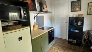 Una cucina compatta con forno a microonde, forno e piccolo frigorifero. C'è un piano di lavoro in legno, una lampada a sospensione e una porta con un piccolo ripiano sopra.