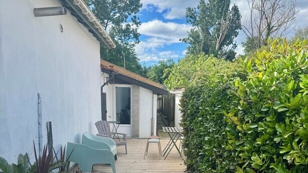 Un sentiero in legno conduce a un edificio bianco con una porta e finestre, immerso nel verde sotto un cielo sereno.