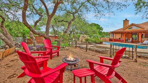 A backyard with a fire pit, red Adirondack chairs, and a swimming pool.
