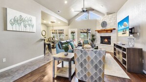 A spacious living room with a fireplace, a dining area, and a kitchen in the background.