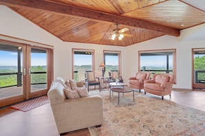 A spacious living room with a high ceiling, large windows, and a view of the outdoors.