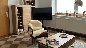 Olohuoneessa on puinen kaappi, taulutelevisio, tuoli, sohvapöytä ja kuviollinen matto.