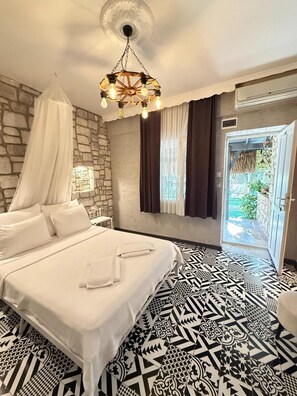 A bedroom with a bed, a stone wall, a patterned floor, a hanging light fixture, and a view through an open door. - Zeren Alaçatı Butik Otel (Cesme)
