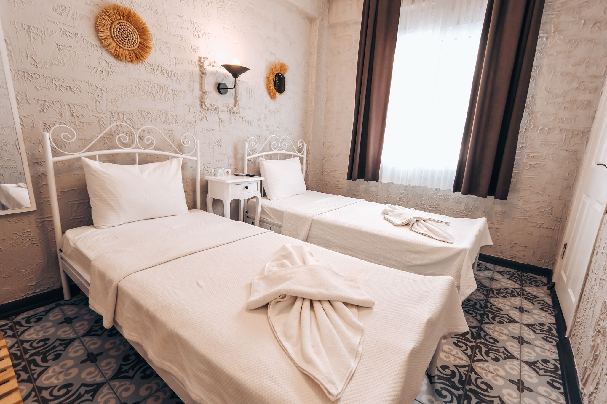 A room with two beds, a small table, and a wall-mounted lamp.