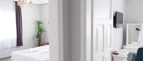 Habitación de hotel con cama, escritorio, silla, planta, espejo y televisor.