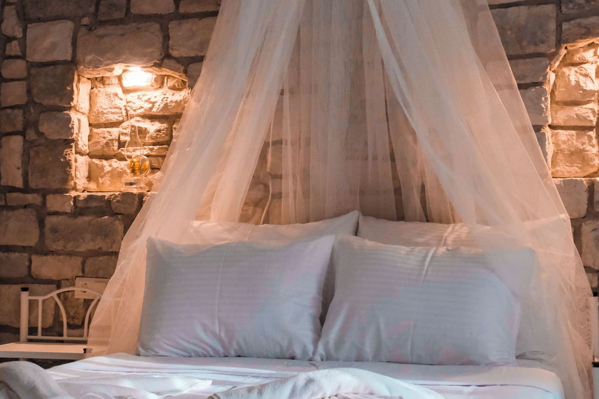 A bed with a canopy, a stone wall, and a hanging light fixture.
