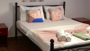 Una cama bien hecha con almohadones decorativos, una mesita de noche y un estante en la pared con objetos pequeños.