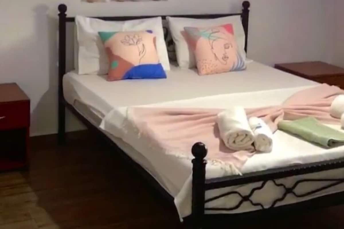A neatly made bed with decorative pillows, a bedside table, and a wall-mounted shelf with small items.