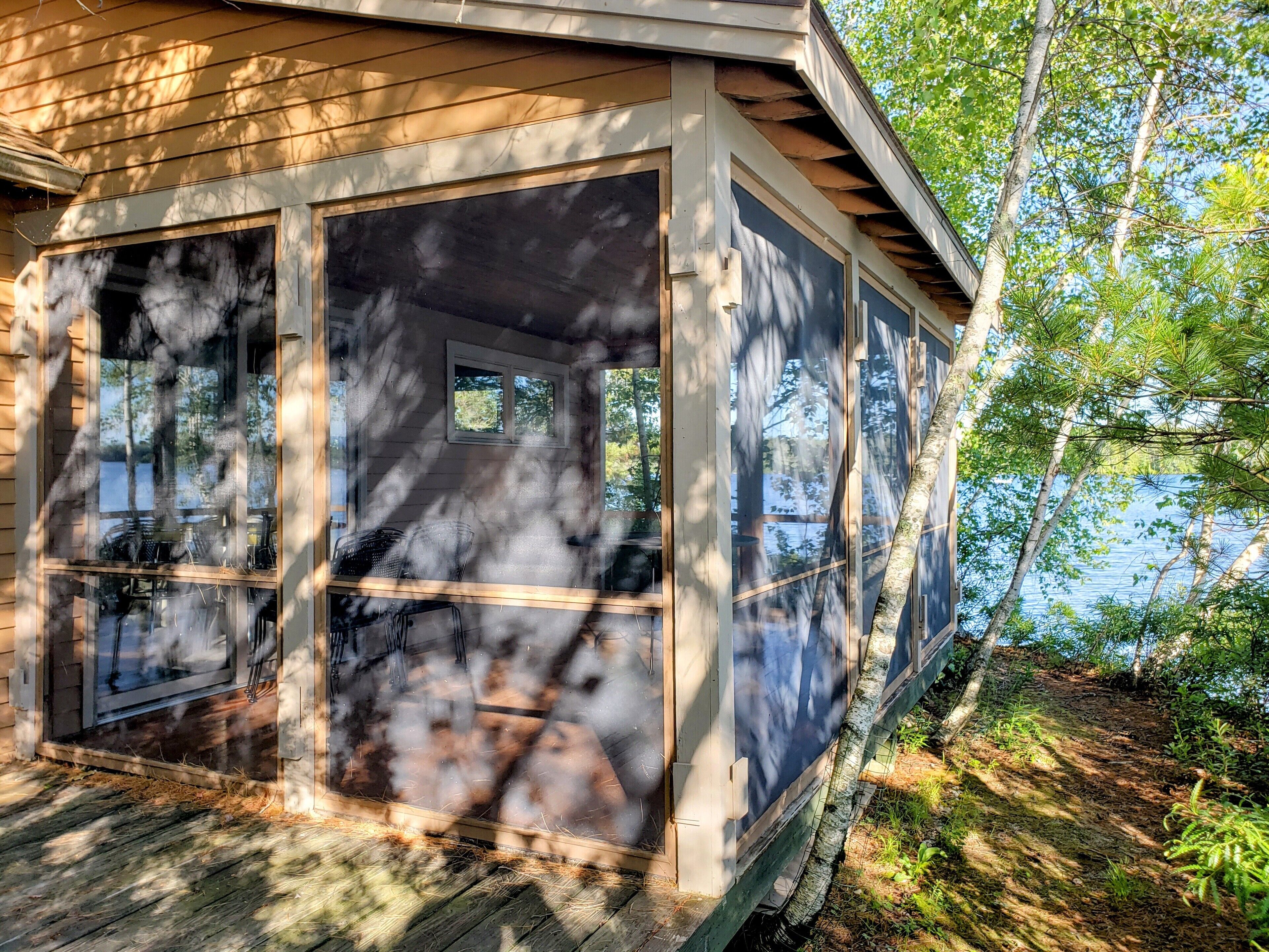 Una cabaña con ventanas amplias, una terraza y vistas del bosque y el agua circundantes.
